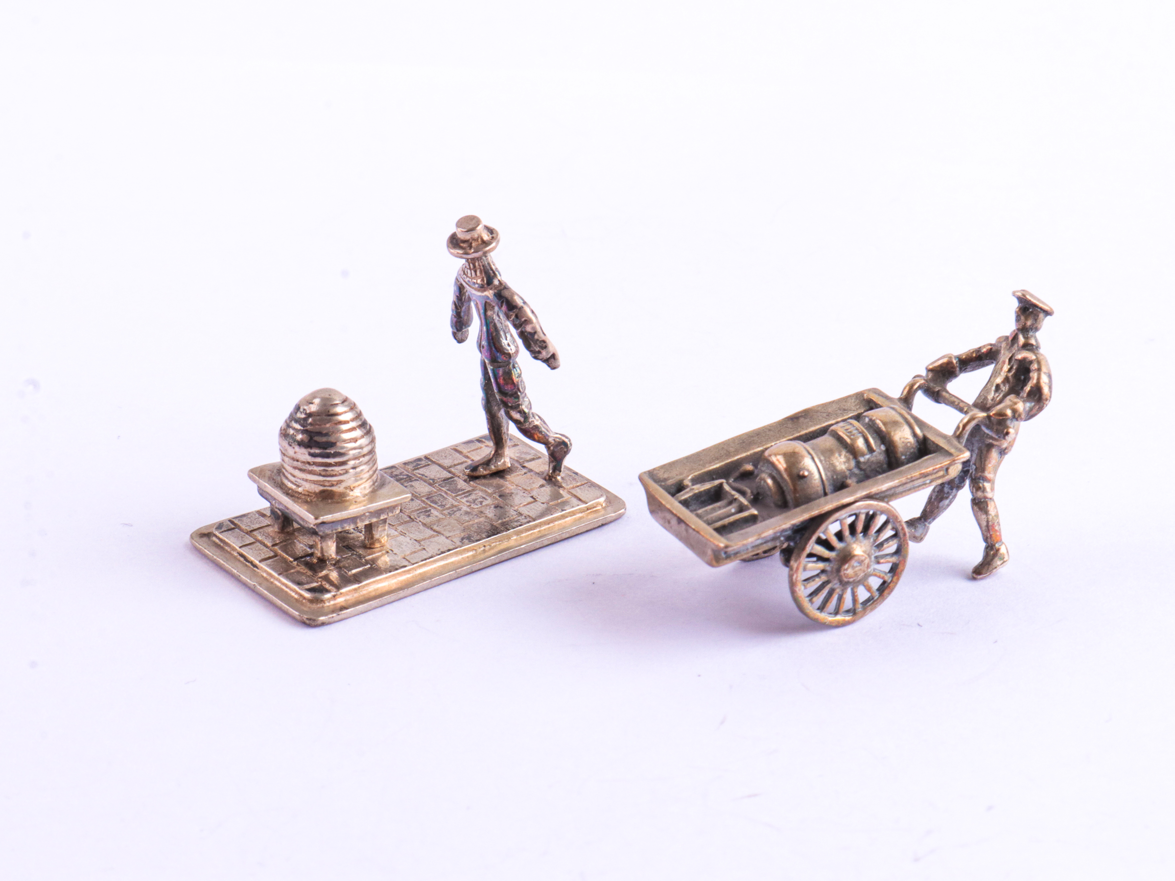 2 Zilveren miniaturen in de vorm van een Imker bij een bijenkorf en een handkar.